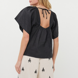Woman wearing a black top with open back and white pants with black patterns on a white background