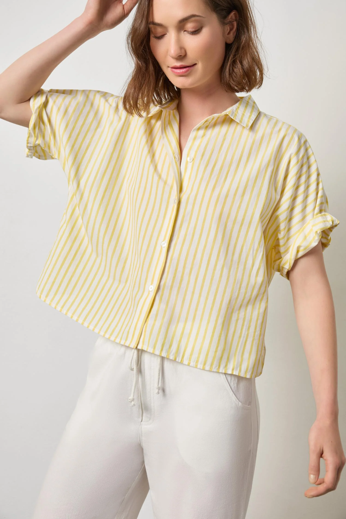 Woman wearing a yellow and white striped shirt with white pants against a plain background