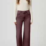 A woman modeling a pair of high-waisted, wide-leg jeans in a dusty plum purple color, paired with a cream ribbed knit sweater and beige pointed-toe heels, against a light gray studio background.