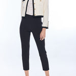 woman in black pants and white jacket with black trim and gold buttons on white background 