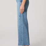 Person wearing light blue jeans and white sneakers on a plain background