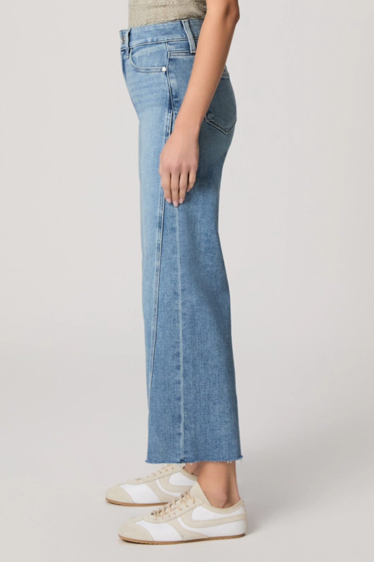 Person wearing light blue jeans and white sneakers on a plain background