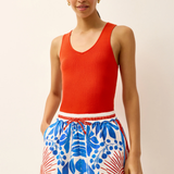 Woman wearing a red sleeveless top and blue floral shorts on a beige background