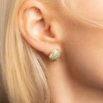 A close-up of a model's ear wearing a small gold stud earring encrusted with clear stones.