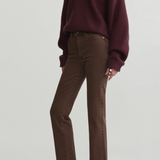 A model wearing a dark burgundy knit V-neck sweater, brown straight-leg jeans, and black pointed-toe flats, photographed against a light gray studio background.