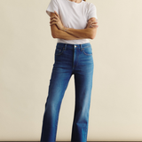 Woman wearing blue jeans and a white t-shirt against a beige background