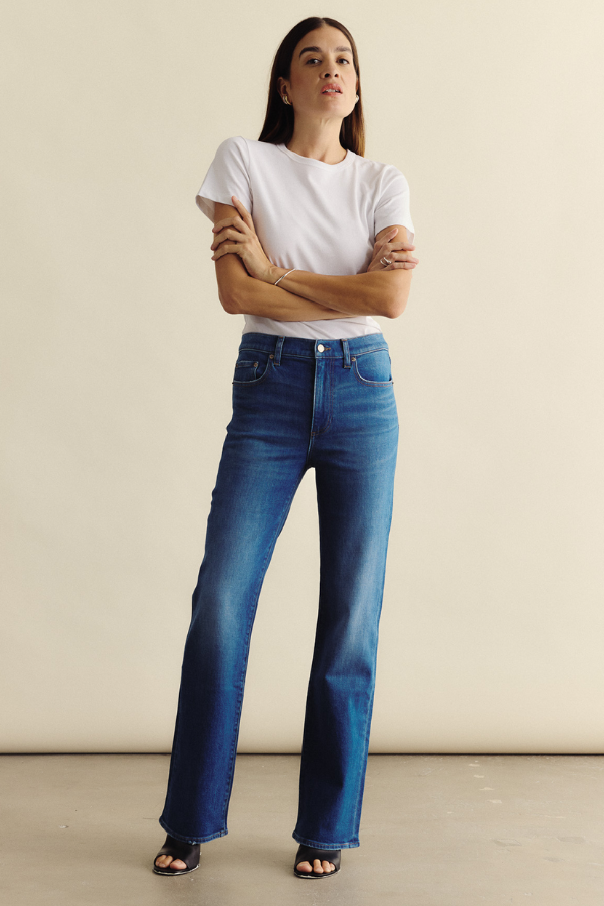 Woman wearing blue jeans and a white t-shirt against a beige background