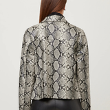 A woman viewed from the back wearing a cropped long-sleeve jacket with a snakeskin pattern in beige, gray, and black, paired with black leather pants, against a light gray studio background.