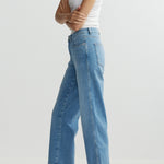 Person wearing blue jeans and a white tank top on a light gray background