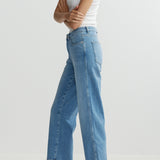 Person wearing blue jeans and a white tank top on a light gray background