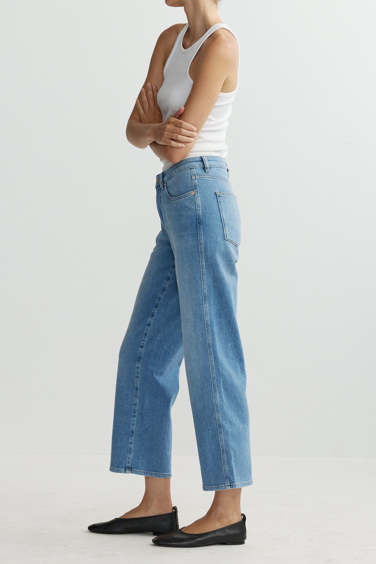 Person wearing blue jeans and a white tank top on a light gray background