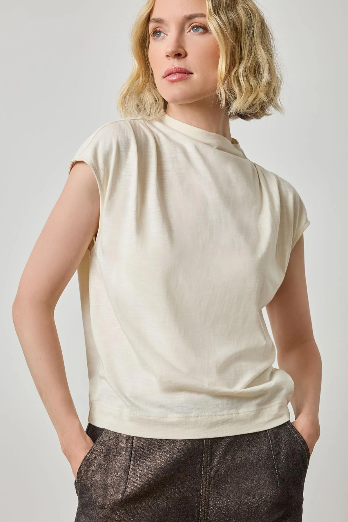 Woman wearing a beige sleeveless top against a plain background