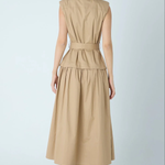 A woman shown from the back wearing a sleeveless beige midi dress with a defined waist and a flared skirt, paired with black ankle boots, against a light gray studio background.