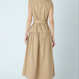 A woman shown from the back wearing a sleeveless beige midi dress with a defined waist and a flared skirt, paired with black ankle boots, against a light gray studio background.