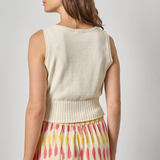 Woman wearing a cream sleeveless top and colorful skirt on a plain background