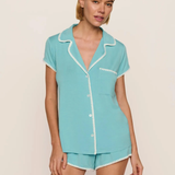 Woman wearing a teal pajama set with white trim on a beige background
