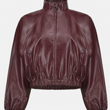 A cropped, long-sleeve jacket in a glossy burgundy faux leather material, featuring a mock neck, front zipper, and elasticized hem and cuffs, shown against a plain light gray background.