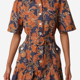 A woman wearing a short-sleeve button-front shirt dress with a ruffled hem and a bold orange floral print on a dark navy background, photographed against a light gray studio backdrop.