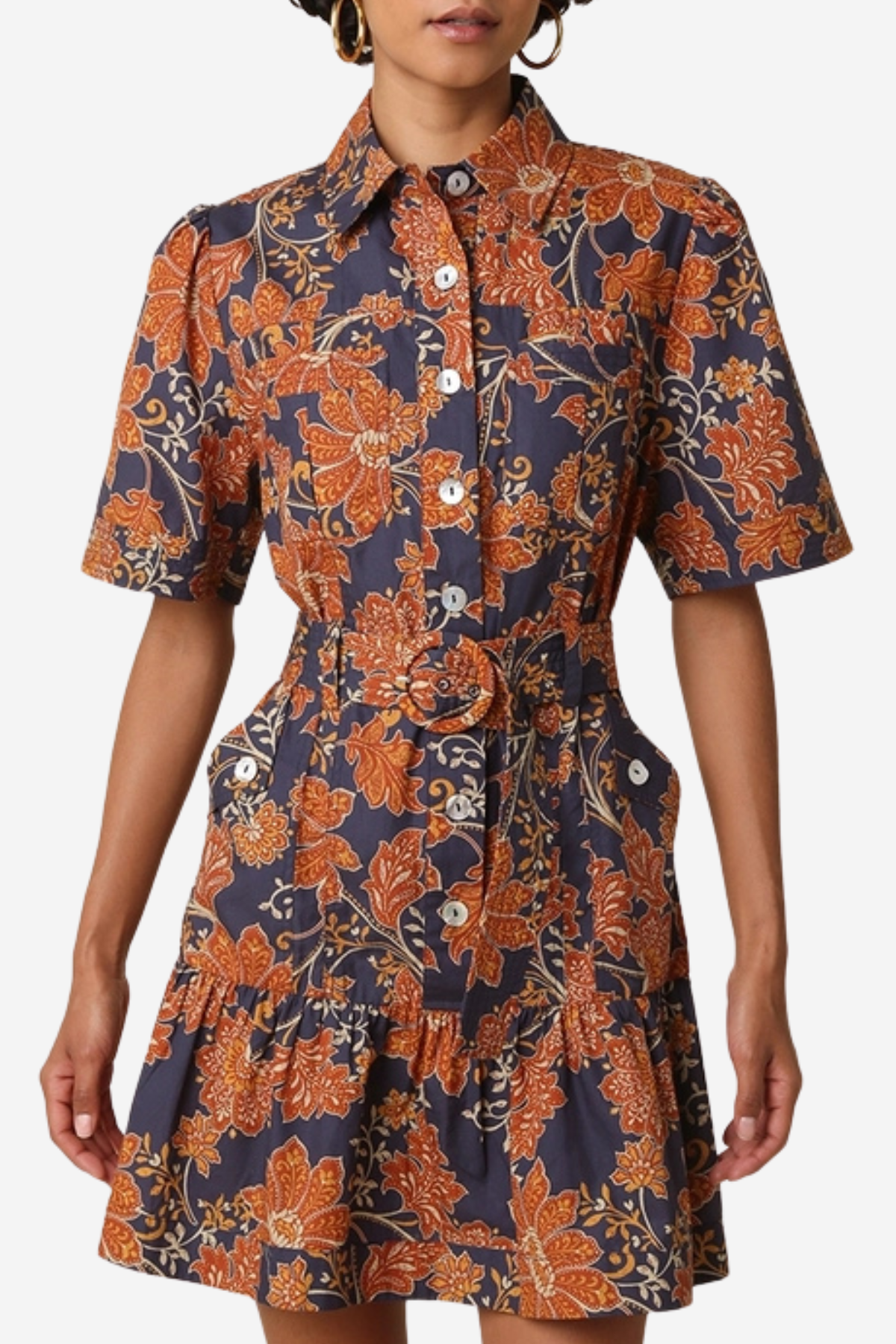 A woman wearing a short-sleeve button-front shirt dress with a ruffled hem and a bold orange floral print on a dark navy background, photographed against a light gray studio backdrop.