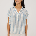 Woman wearing a striped shirt and white pants against a plain background
