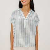 Woman wearing a striped shirt and white pants against a plain background