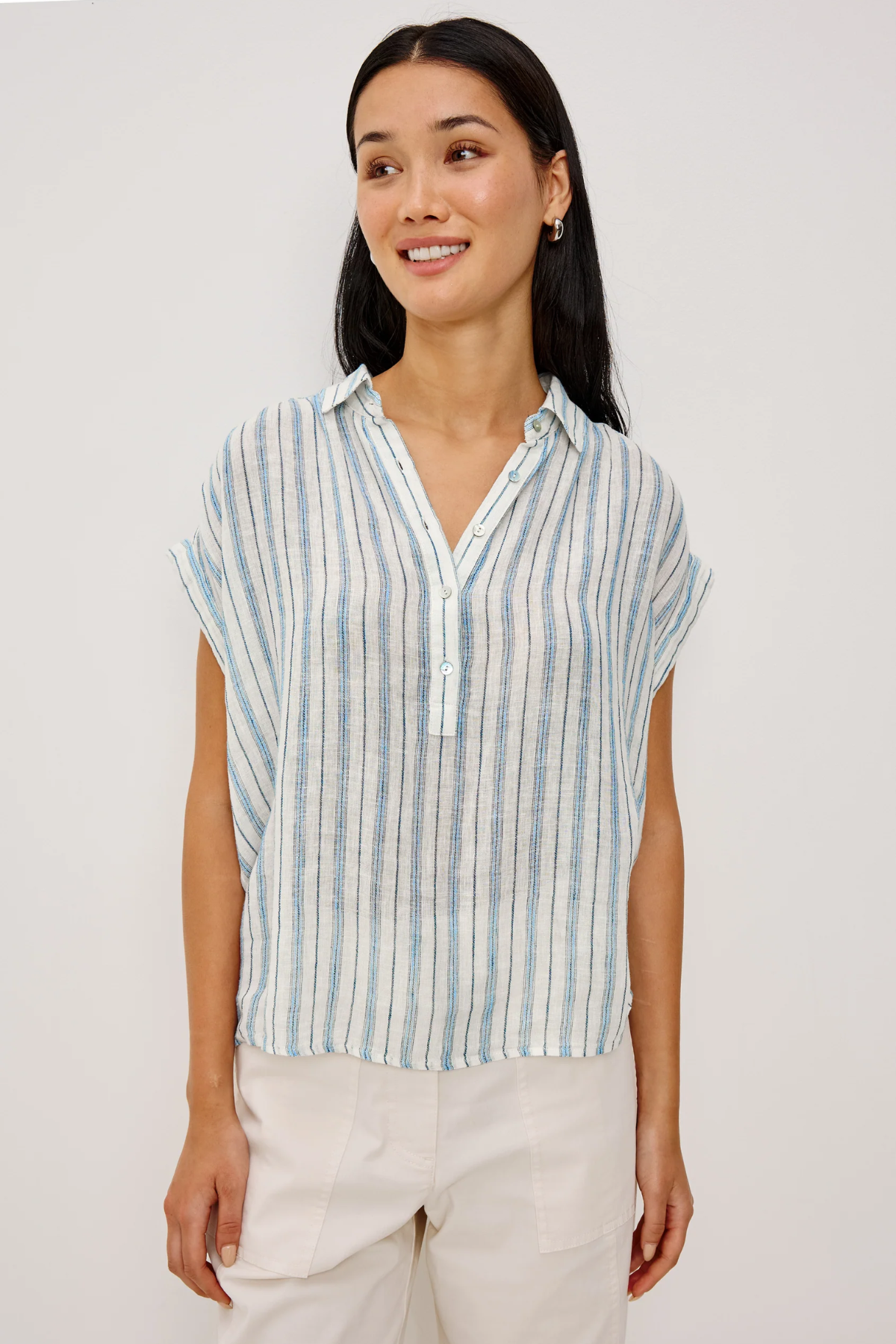 Woman wearing a striped shirt and white pants against a plain background