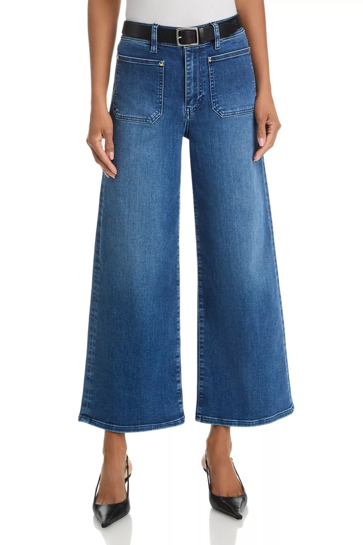 A model wearing a pair of blue wide-leg cropped denim jeans with a black belt, styled with black pointed-toe heels against a white studio background.