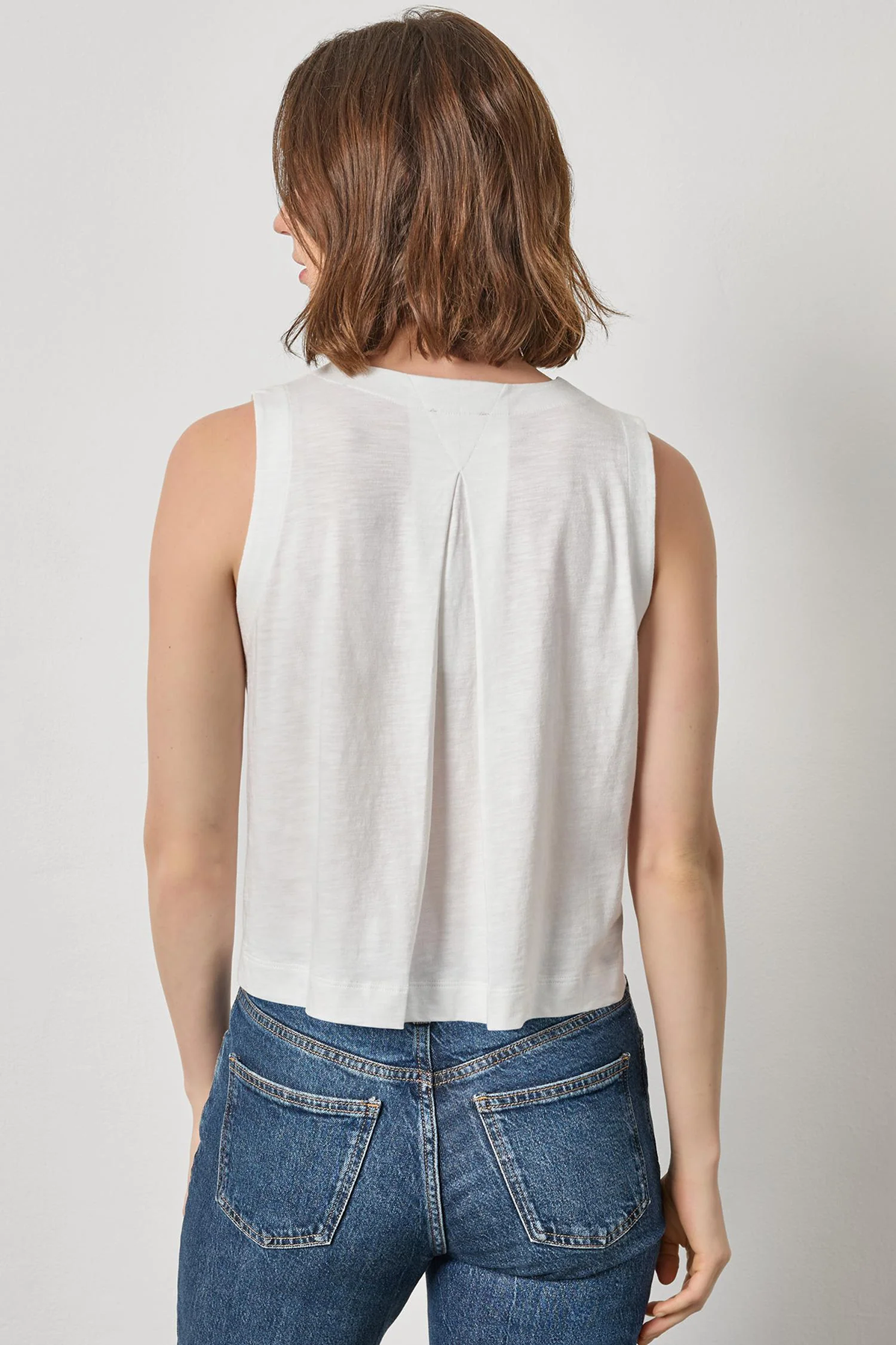 Person wearing a white sleeveless top and blue jeans on a plain background