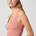 Woman wearing a pink ribbed tank top against a plain background