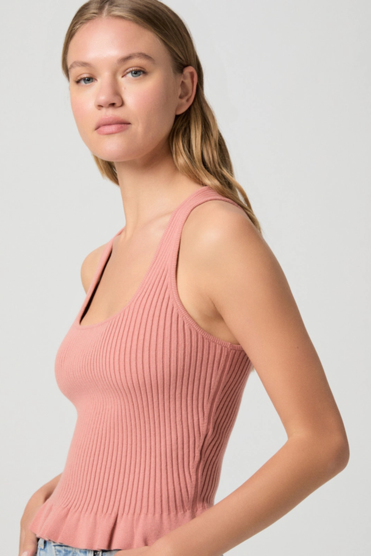 Woman wearing a pink ribbed tank top against a plain background