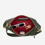 An olive green leather handbag shown open against a light gray background, revealing a deep red interior lined with sunglasses, keys, and a small white item.