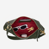 An olive green leather handbag shown open against a light gray background, revealing a deep red interior lined with sunglasses, keys, and a small white item.