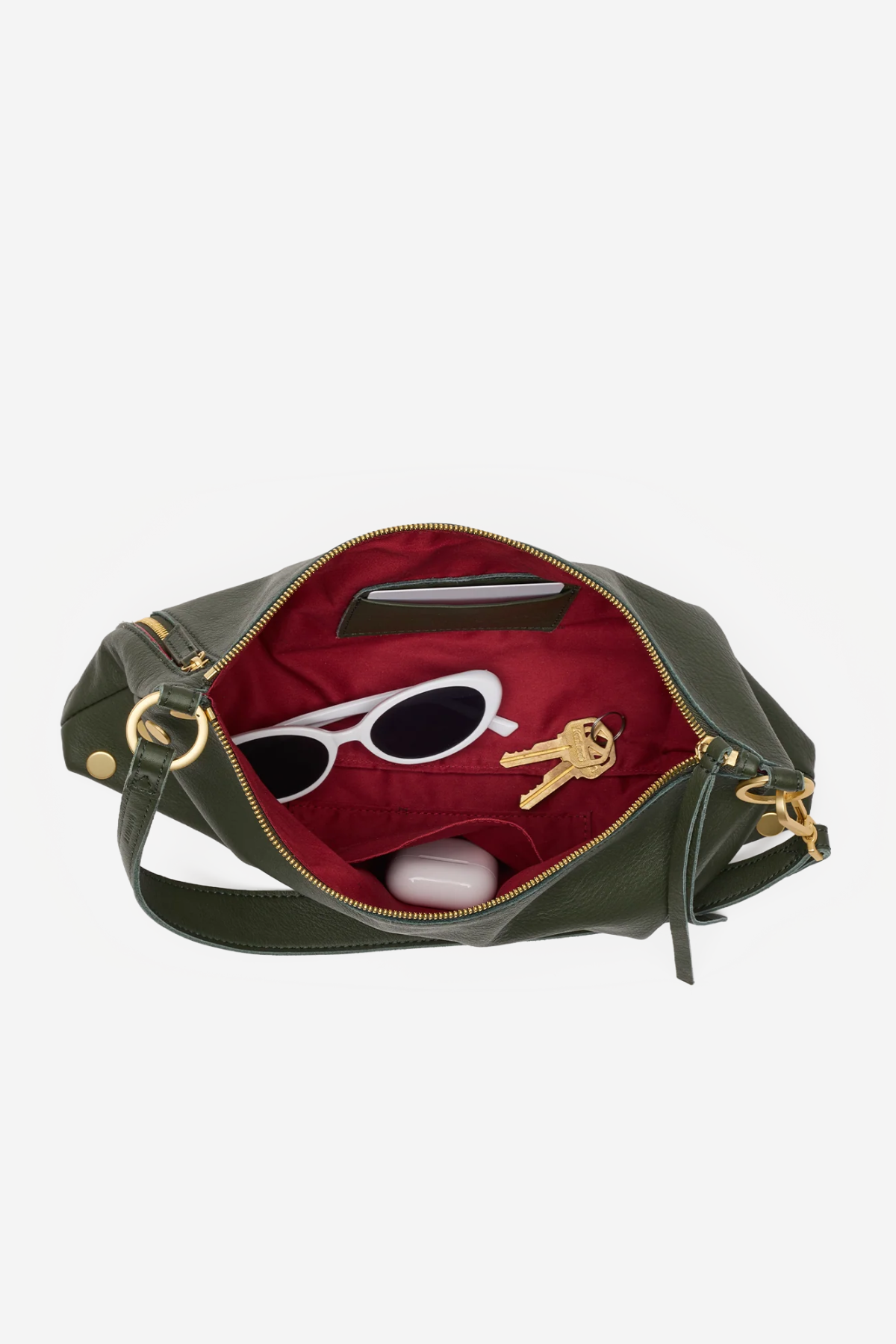 An olive green leather handbag shown open against a light gray background, revealing a deep red interior lined with sunglasses, keys, and a small white item.
