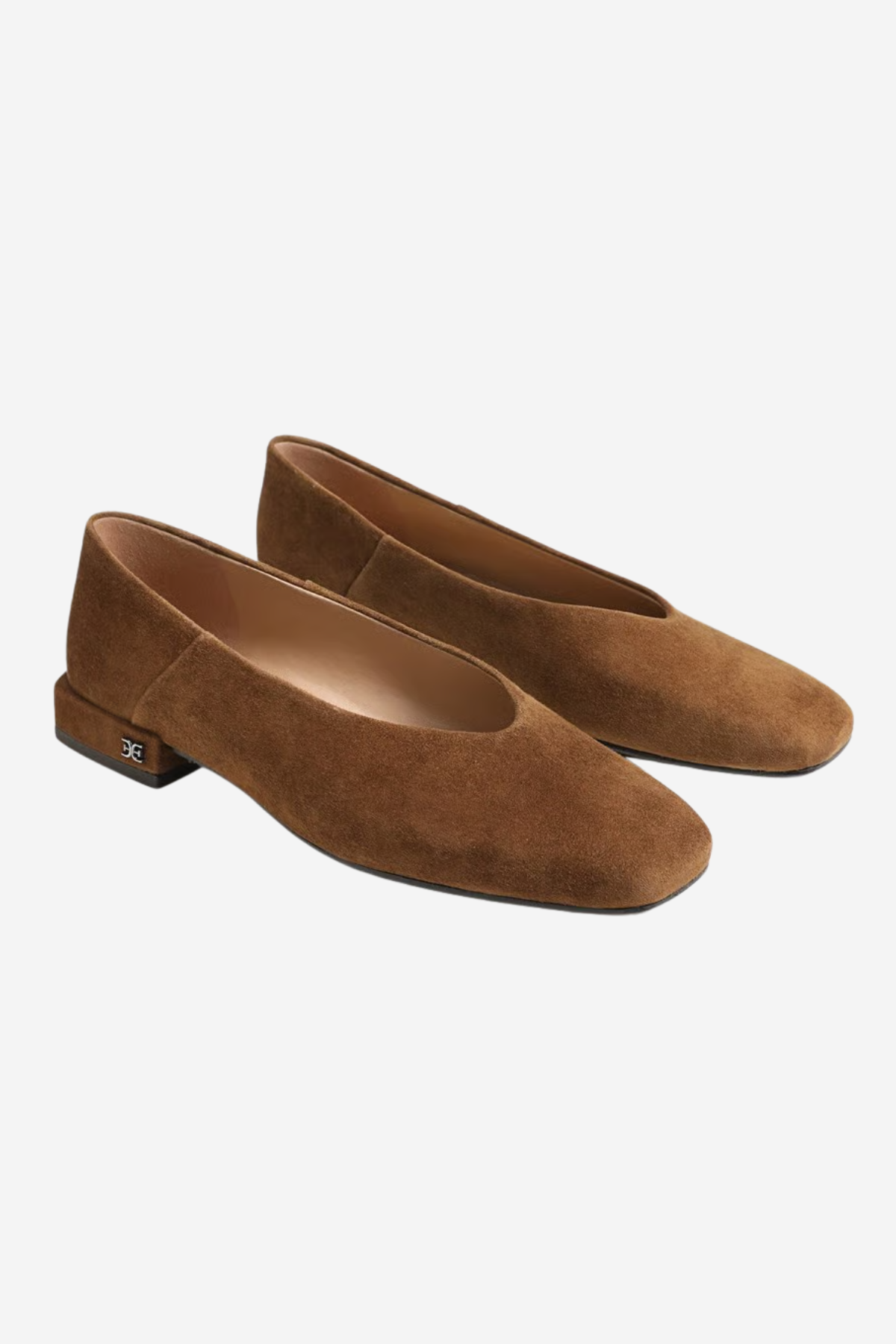 A pair of women's flat shoes in brown suede, featuring a low block heel and a small metallic brand plaque on the outer side, set against a plain light gray background.