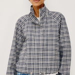 A woman wearing a navy, white, and gray plaid long-sleeve jacket with a high stand-up collar, paired with light blue jeans, against a plain light gray background.