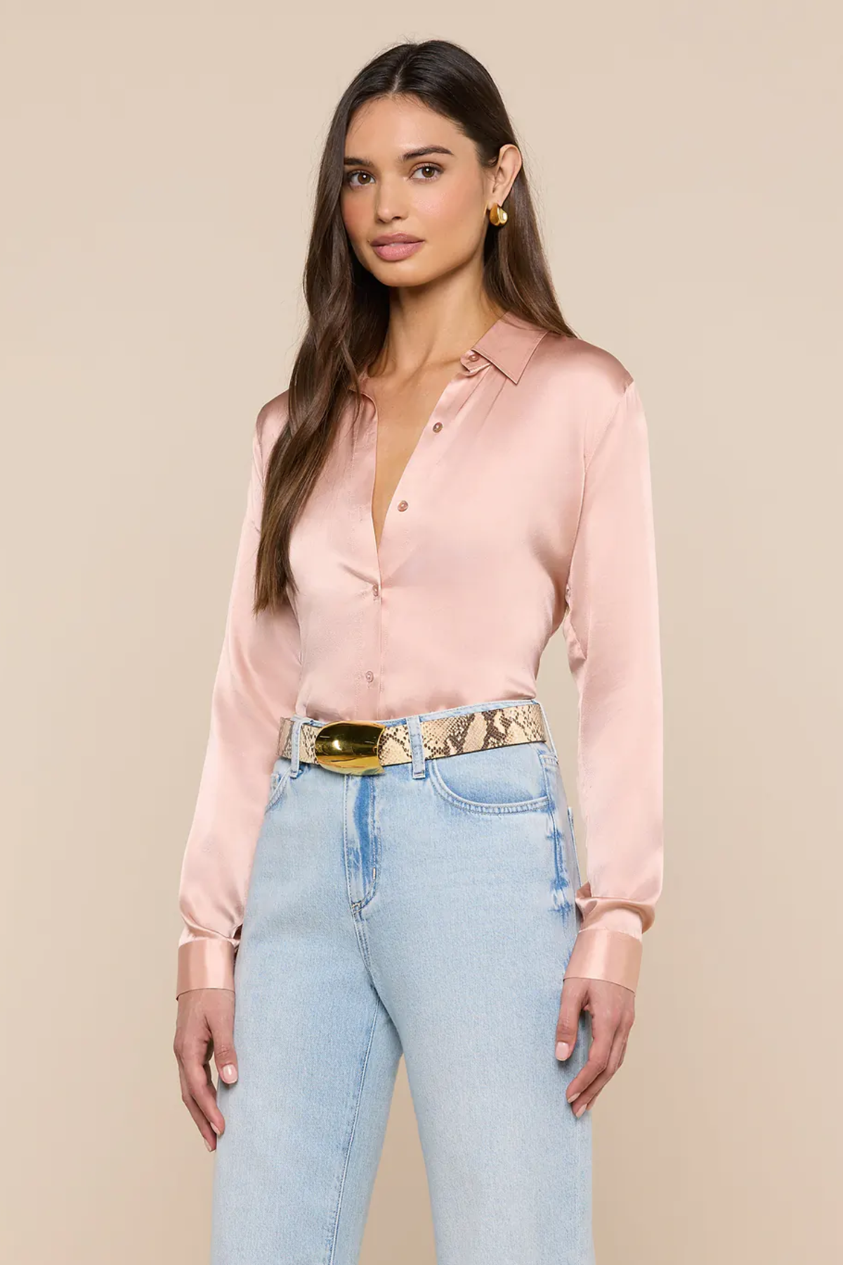 Woman wearing a light pink blouse and light blue jeans with a beige background