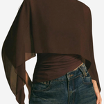 A woman wearing a dark brown draped long-sleeve top with a wide boat neckline and sheer side panels, paired with blue jeans, against a plain light background.