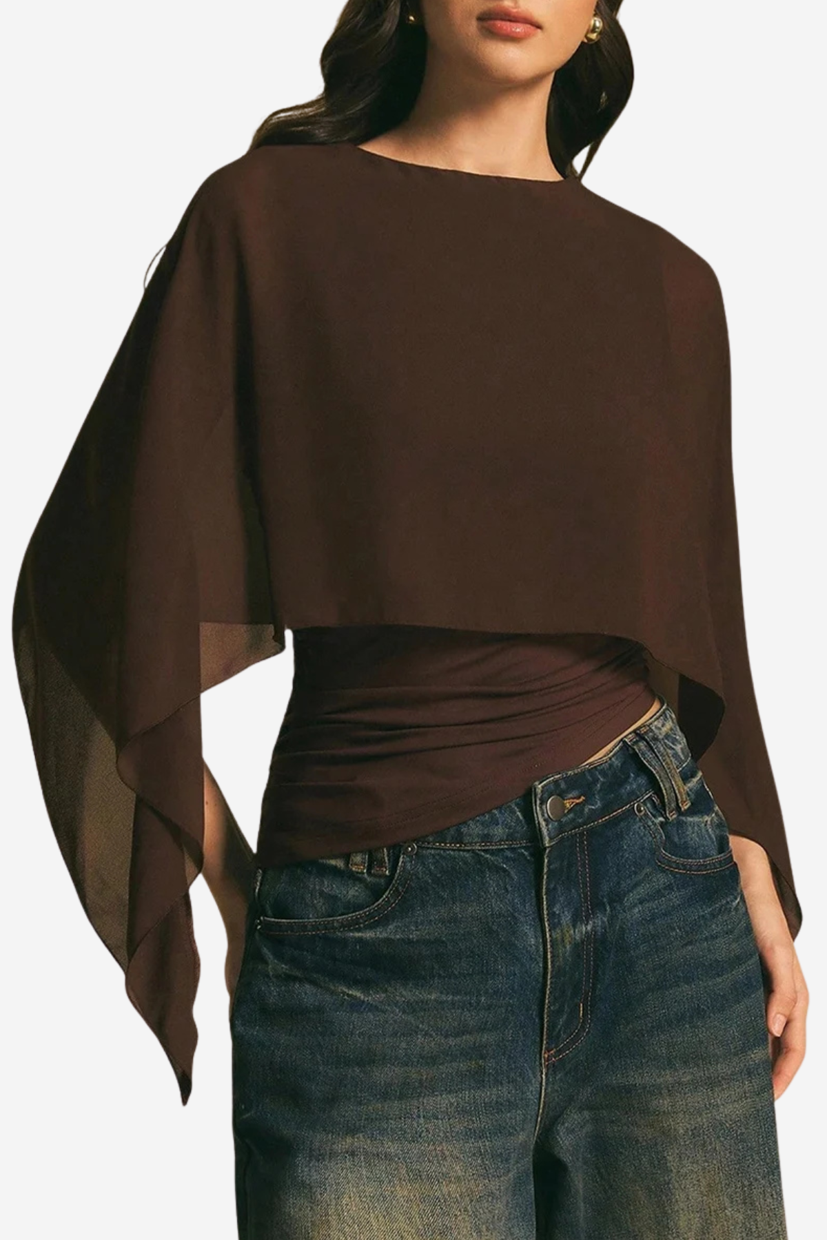 A woman wearing a dark brown draped long-sleeve top with a wide boat neckline and sheer side panels, paired with blue jeans, against a plain light background.