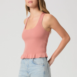 Woman wearing a pink ribbed tank top and light blue jeans on a plain background