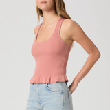 Woman wearing a pink ribbed tank top and light blue jeans on a plain background