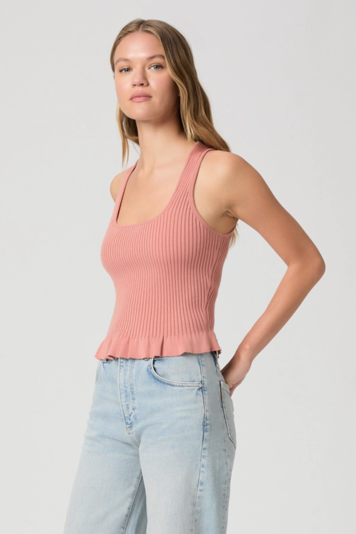 Woman wearing a pink ribbed tank top and light blue jeans on a plain background