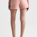 A person shown from the back wearing light pink denim shorts, a gray top, and dark brown sandals against a plain light gray studio background.