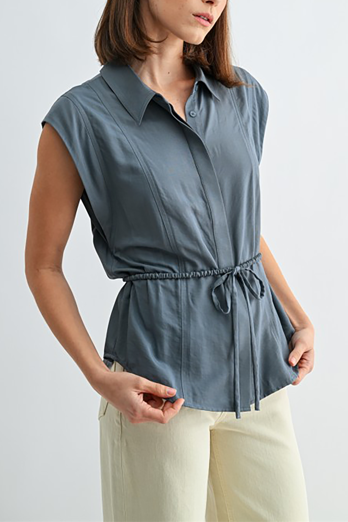 Woman wearing a sleeveless blue shirt with a tie waist on a light gray background