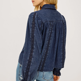 A woman shown from the back wearing a dark blue denim long-sleeve blouse with black lace trim along the shoulders, sleeves, and cuffs, paired with light blue jeans against a plain white background.