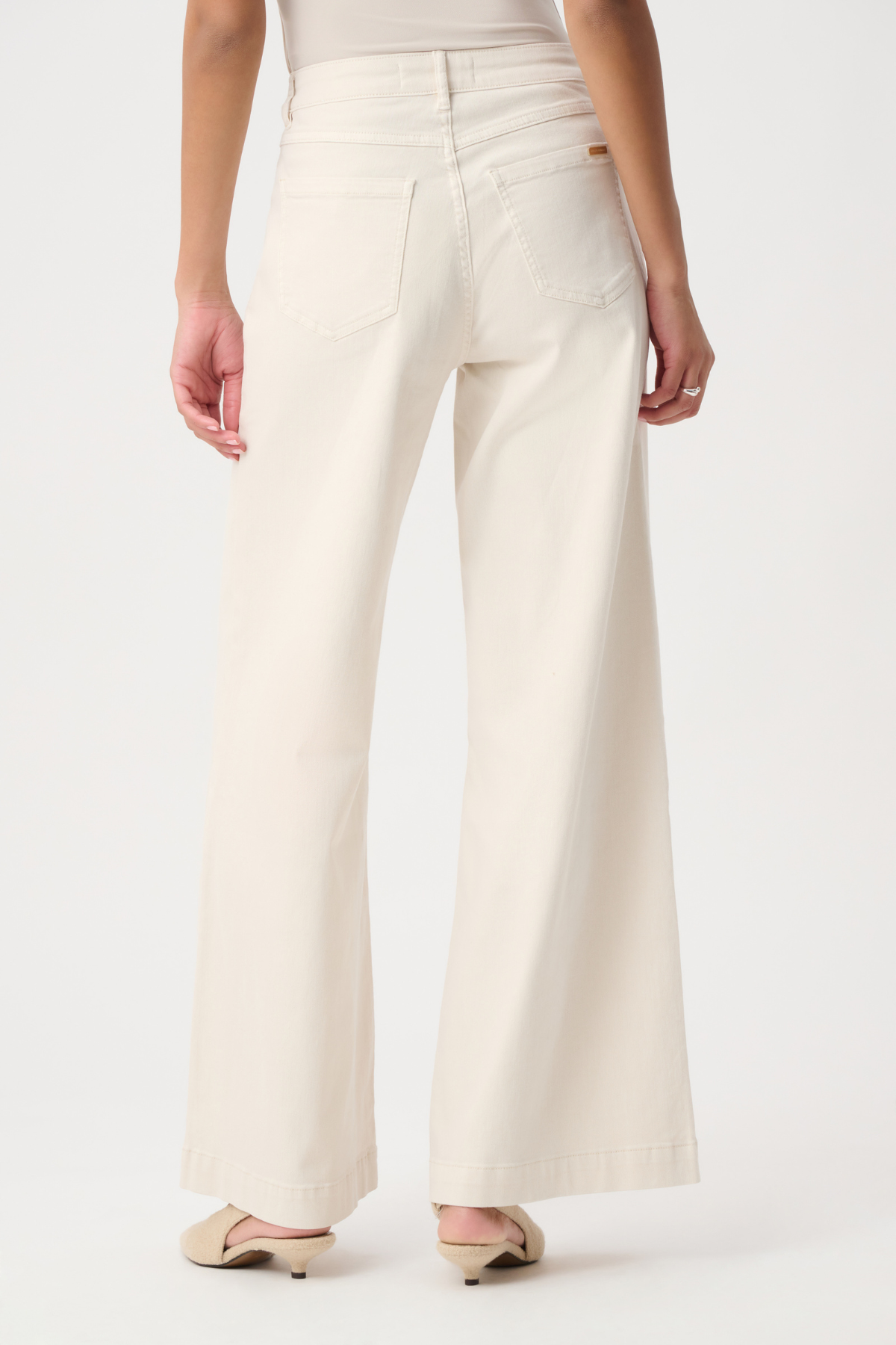 A person shown from the back wearing off-white wide-leg pants with a beige top and beige flat shoes, photographed against a plain light background.