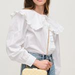 Woman wearing a white blouse with ruffled details and holding a yellow quilted handbag.