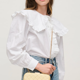 Woman wearing a white blouse with ruffled details and holding a yellow quilted handbag.