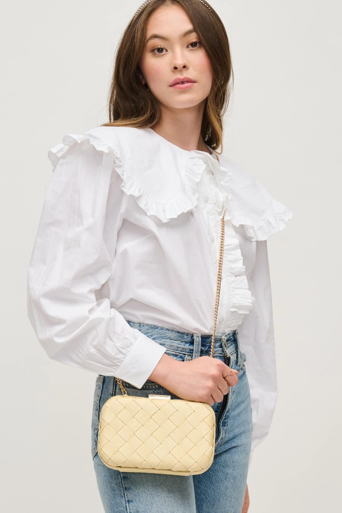 Woman wearing a white blouse with ruffled details and holding a yellow quilted handbag.