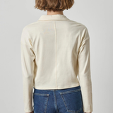 A model viewed from the back wearing a cream-colored long-sleeve knit top and blue jeans against a light gray studio background.