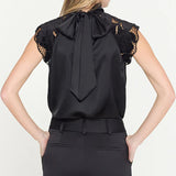 Black sleeveless top with lace details and a bow tie, worn by a person on a white background